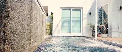 A swimming pool with a stone wall on one side and a white building with a glass door in the background.