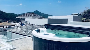 Una terraza con jacuzzi, barandillas de cristal y vistas a la montaña.