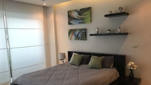 Un dormitorio moderno con una cama grande, una mesita de noche con lámpara y estantes en la pared con objetos decorativos.