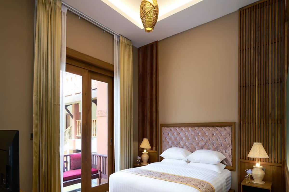 Une chambre d’hôtel avec un grand lit, deux tables de chevet avec des lampes, une télévision, un panier de fruits et une vue sur un balcon.