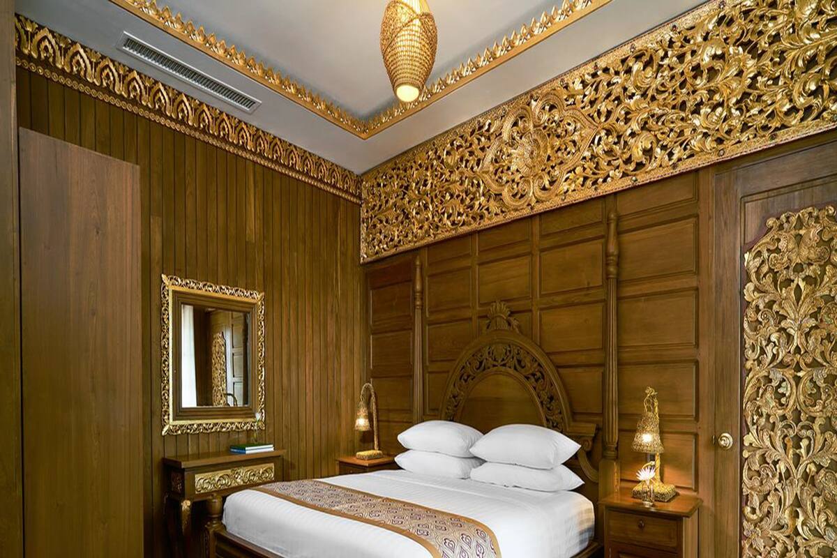 Un grand lit avec une tête de lit en bois, deux tables de chevet avec des lampes, un miroir et des boiseries murales décoratives.