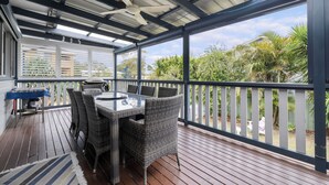 Een overdekt terras met een tafel, stoelen, een plafondventilator en uitzicht op groen.