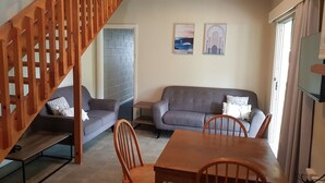 A living room with a grey sofa, two armchairs, a wooden dining table, and a staircase.