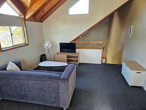 Habitación estilo loft con sofá, una mesita, televisor y ventilador.