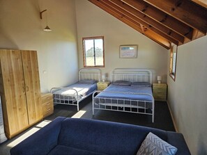 Un dormitorio con dos camas individuales, un armario de madera, un sofá y un techo inclinado.