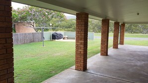 A covered patio area with brick columns, a grassy lawn, and a wooden fence in the background.