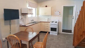 A compact kitchen with white cabinets, a stove, and a sink. There is a dining table with chairs and a television mounted on the wall.