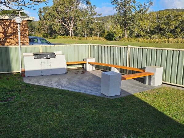 Un área de patio al aire libre con una parrilla de barbacoa integrada, un banco de madera y una maceta de piedra.