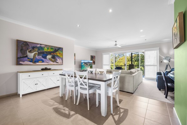 A spacious dining area with a white table and chairs, a white cabinet, and a painting on the wall.