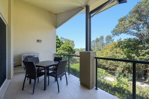 A balcony with a table and chairs, an air conditioning unit, and a view of trees and greenery.