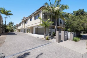 A two-story residential building with a covered driveway and palm trees.