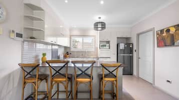 Une cuisine moderne avec un îlot central, quatre tabourets de bar, un four à micro-ondes, un réfrigérateur et un tableau accroché au mur.