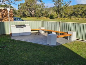 Un espace patio extérieur comprenant un barbecue intégré, un banc en bois et un bac à fleurs en pierre.