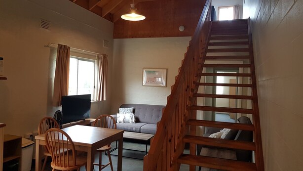 Ein gemütliches Zimmer mit einer Holztreppe, einem Essbereich mit Tisch und Stühlen, einem Sofa und einem Fernseher.