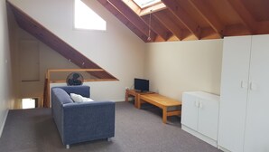 Ein gemütlicher Raum mit schrägen Wänden, einer Couch, einem kleinen Schreibtisch mit Computer und einem Kleiderschrank.