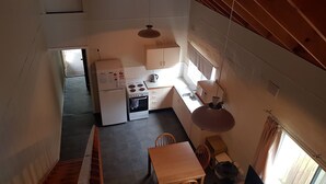 Eine kompakte Küche mit Kühlschrank, Herd und Spüle. Ein Holztisch und Stühle stehen in der Nähe des Fensters.