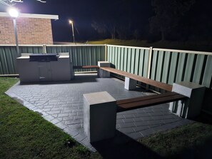 Un espace extérieur aménagé en terrasse, doté d’un barbecue intégré, de sièges et d’une clôture.