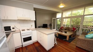 Una cocina compacta con armarios blancos, microondas y estufa. Hay un comedor con mesa de madera y un sofá.
