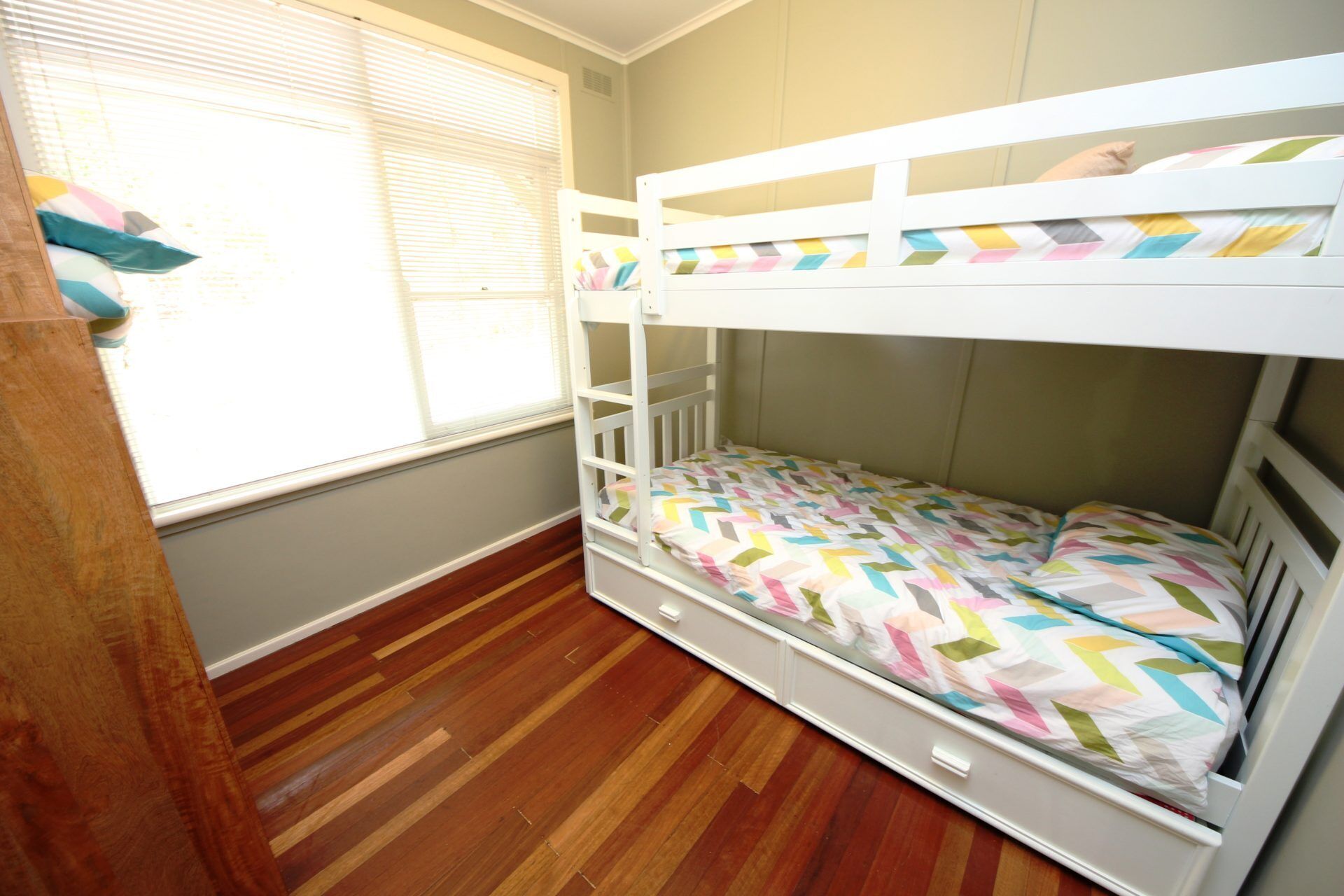 Una cama litera con un edredón de diseño colorido en patrón de estampilla, piso de madera y una ventana con persianas.