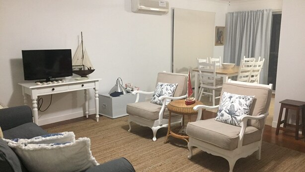 Sala de estar con televisor, escritorio, dos sillones, una mesa de comedor con sillas y un ventilador de techo.