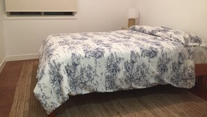 Un dormitorio con cama, ventana, un cuadro y una mesita de noche.