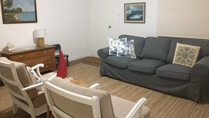 Una sala de estar con un sofá gris, dos sillones blancos, un aparador de madera y una puerta.