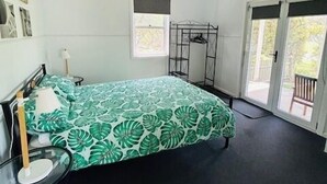 Une chambre à coucher comprenant un lit, un ventilateur de plafond, une fenêtre et une porte donnant sur un espace extérieur.