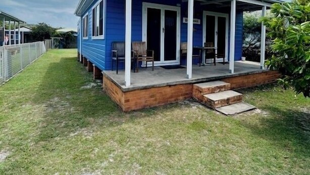 Une maison de plain-pied à l’extérieur bleu, dotée d’un porche couvert avec des chaises et d’une terrasse en bois.