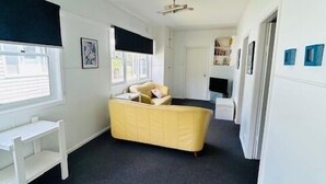 Une pièce spacieuse avec un canapé jaune, un bureau blanc et un ventilateur de plafond.