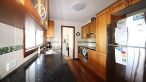 A kitchen with wooden cabinets, a stainless steel refrigerator, a black countertop, and a window with a view. - Kookaburra Cottage 71 Straight Hat Head (Hat Head)