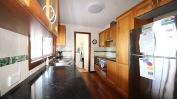 A kitchen with wooden cabinets, a stainless steel refrigerator, a black countertop, and a window with a view.