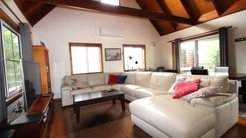 A spacious living room with a high ceiling, large windows, and a wooden ceiling beam.