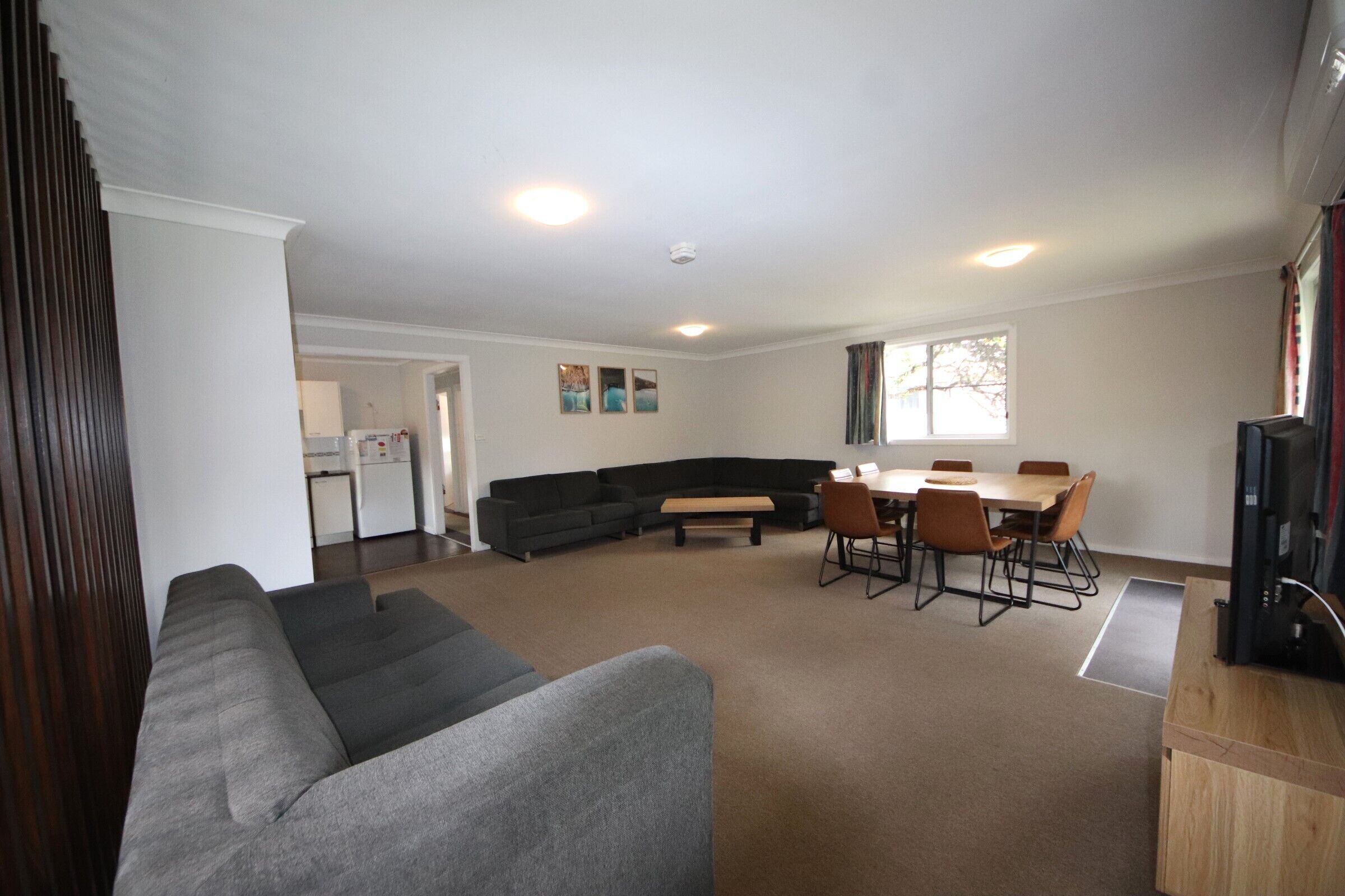 A spacious living area with a sectional sofa, a dining table with chairs, and a kitchen in the background.