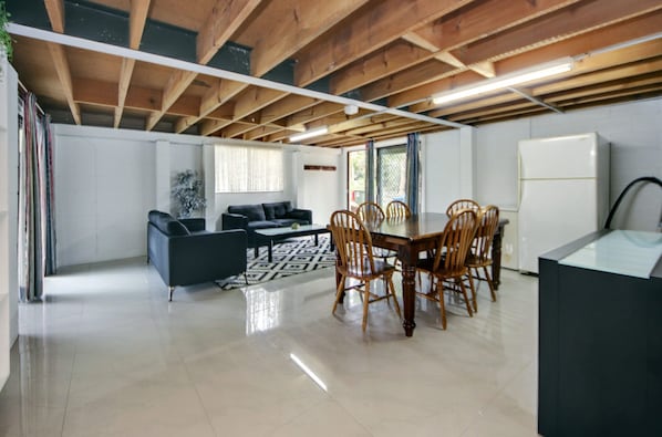 Amplia sala de estar con mesa de comedor, sillas, sofá y área de cocina con refrigerador.