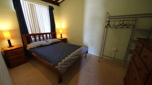 Ein Schlafzimmer mit einem Bett, zwei Nachttischen, einer Lampe, einem Kleiderschrank und einem Kleiderständer.