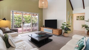 A spacious living room with a large TV, comfortable seating, and a view through glass doors to an outdoor area with a patio.