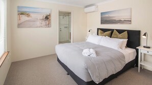 A bedroom with a bed, a nightstand, a wall-mounted air conditioner, and two framed pictures.