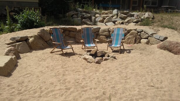 Un espace extérieur sablonneux avec trois chaises de plage rayées et un mur de pierre.
