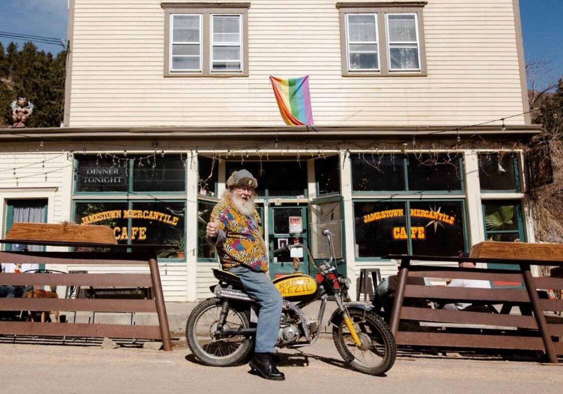 Iemand zit op een motorfiets voor een gebouw met een bord waarop staat 'JAMESVILLE MERCANTILE CAFE'.