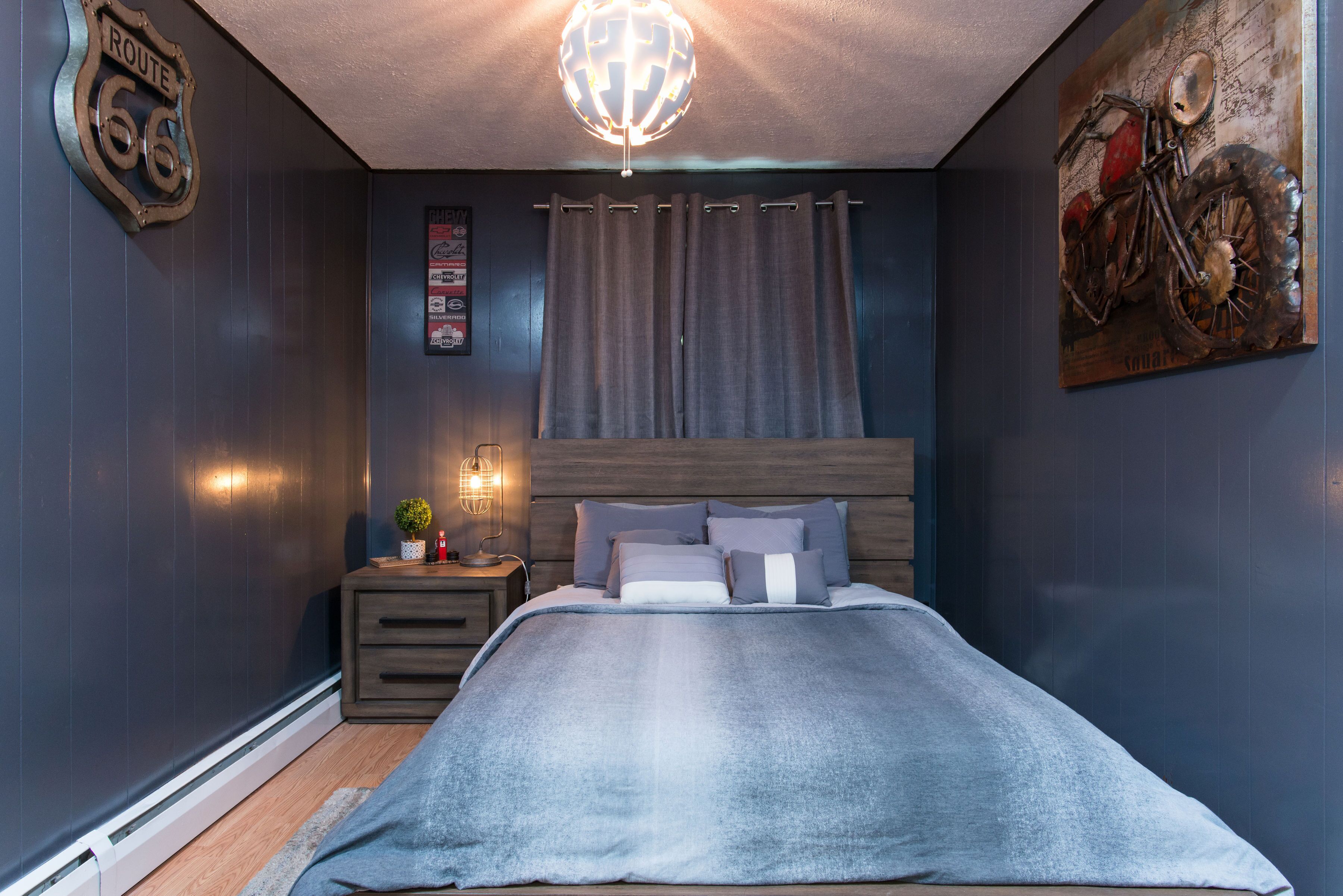Une chambre à coucher comprenant un lit, une table de chevet, une lampe et un tableau représentant une moto accroché au mur.