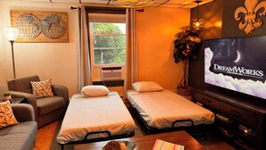 A cozy room with two single beds, a sofa, a TV displaying 'DreamWorks Animation SKG', and a window with curtains. - Charming apt -2 Bedroom -Close to Beach/Sleeps 6 (Ipswich)