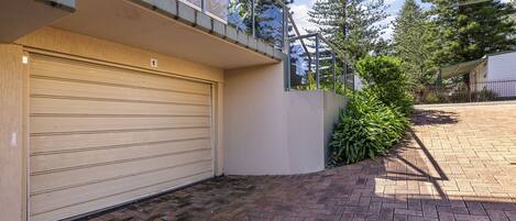 A residential garage with a closed garage door, a brick pathway leading to the entrance, and a small garden area with greenery.
