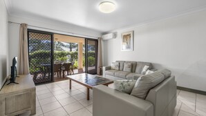 A modern living room with a sofa, coffee table, and TV stand. There is a sliding glass door leading to an outdoor area with a table and chairs. - All Linen Included * Center of Town * BBQ *Air Con * Private Covered Patio* (South West Rocks)