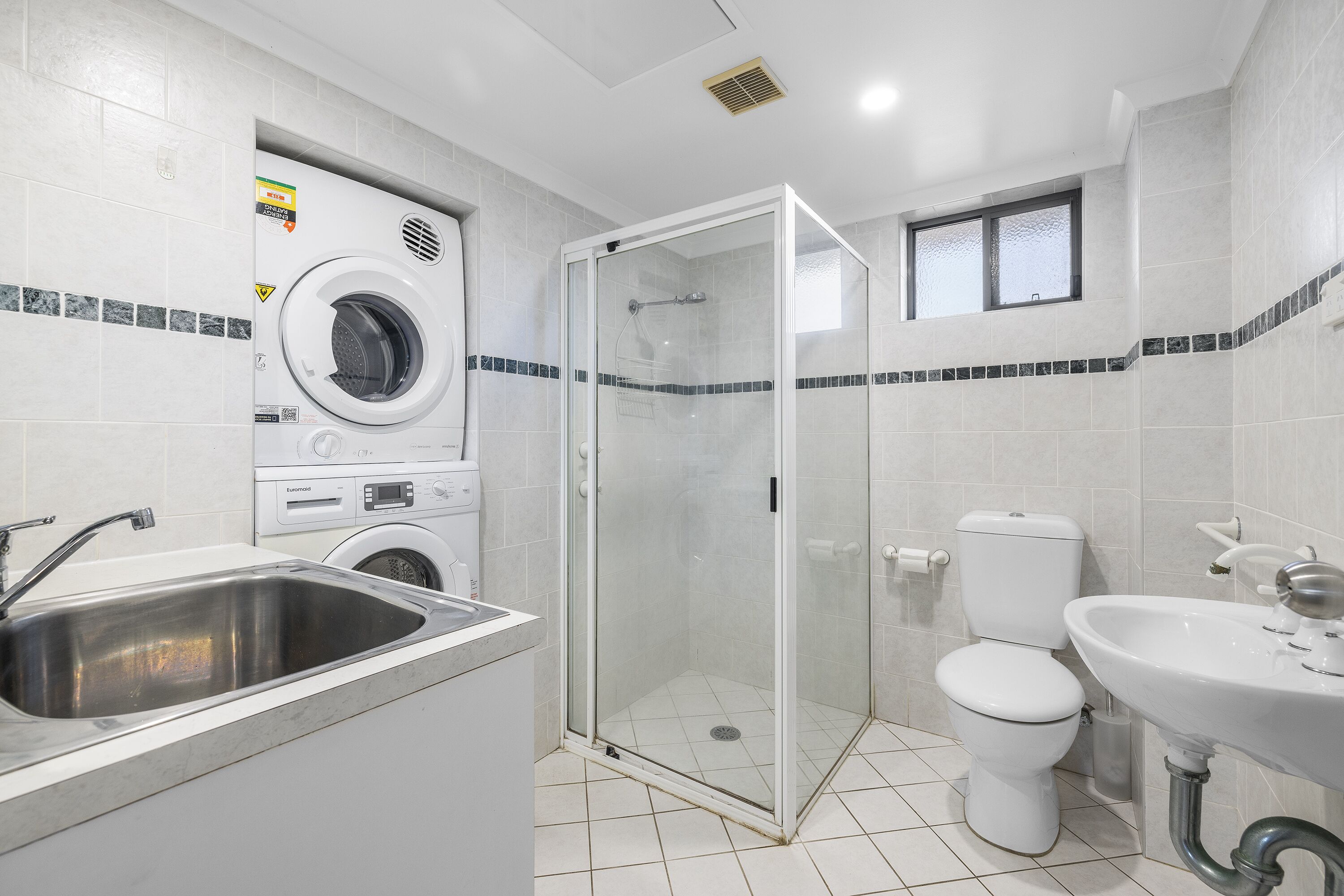 A modern bathroom with a glass-enclosed shower, a toilet, a sink, and a washing machine.