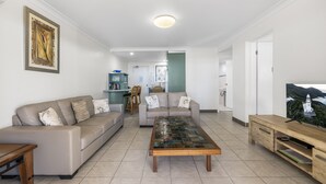 A modern living room with a beige sofa, a wooden coffee table, and a TV on a wooden stand. - All Linen Included * Center of Town * BBQ *Air Con * Private Covered Patio* (South West Rocks)