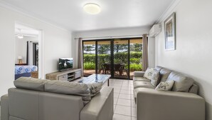 A living room with a sofa, TV, and a table. There is a sliding glass door leading to a patio with a table and chairs. - All Linen Included * Center of Town * BBQ *Air Con * Private Covered Patio* (South West Rocks)