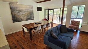 A spacious living room with a wooden dining table, a blue sofa, and a large painting on the wall. - Comfortable air conditioned, pet friendly holiday home with large open... (South West Rocks)