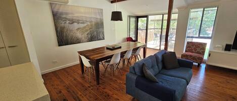 A spacious living room with a wooden dining table, a blue sofa, and a large painting on the wall.