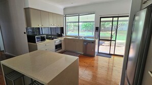 A modern kitchen with a large island, built-in appliances, and a sliding glass door leading to a backyard. - Comfortable air conditioned, pet friendly holiday home with large open... (South West Rocks)