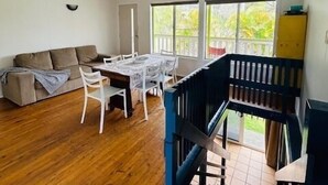 A spacious living area with a wooden floor, a sofa, a dining table with chairs, and a staircase.